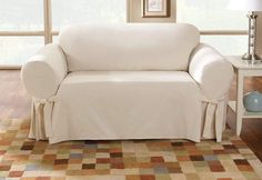 a white couch sitting on top of a wooden floor next to a lamp and window