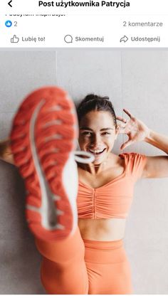 a woman in an orange sports bra top is smiling and holding her shoe up to the side