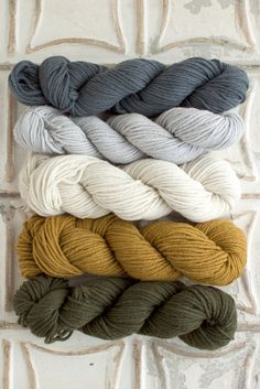 four skeins of yarn in various colors on a white brick wall with leaves