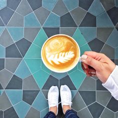 a person holding a cup of coffee on top of a tiled floor next to their feet