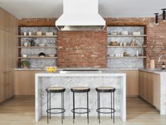 an open kitchen with brick walls and marble counter tops, stools at the island