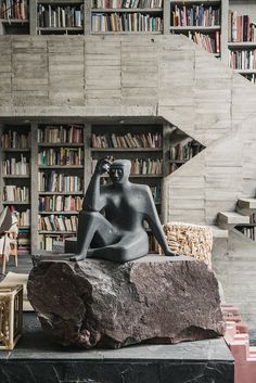 a statue sitting on top of a rock in front of a book shelf filled with books