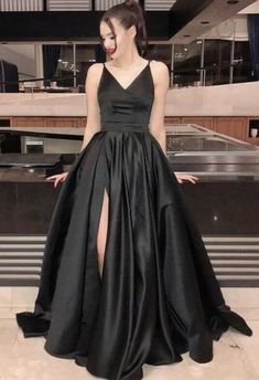 a woman standing in front of a counter wearing a black dress with high slits