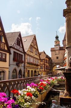 colorful flowers line the side of buildings in an old european town with water running through them