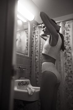 a woman standing in front of a bathroom sink with her hands on her head and looking into the mirror