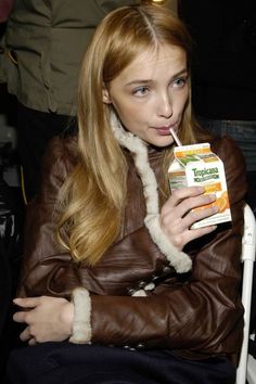 a woman sitting in a chair drinking from a carton