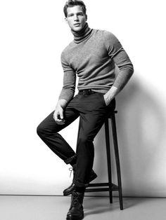 a man sitting on top of a wooden chair next to a white wall in black and white