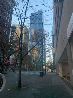 an empty city street with tall buildings in the back ground and bare trees on both sides