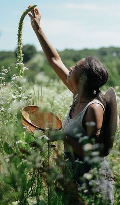 a woman in a field picking flowers from a plant with her arm up to the sky