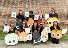 a group of women holding up paper cutouts with faces on them and eyes drawn on them