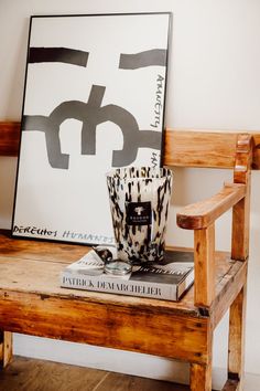 a wooden chair sitting next to a painting and a cup on top of a book