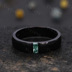 a black wedding band with a green stone in the center