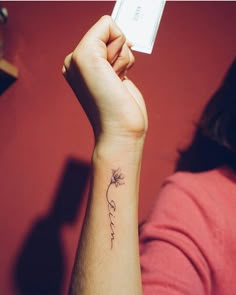 a woman with a small flower tattoo on her wrist holding up a card in front of her face