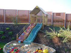 an outdoor play area with a slide and sandpit in the middle, next to a wooden fence