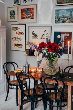 a dining room table with chairs and pictures on the wall above it, along with vases filled with flowers