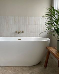 a large white bath tub sitting next to a wooden table and potted palm tree