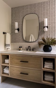 a bathroom vanity with two sinks and a large mirror above it, in front of a patterned wall