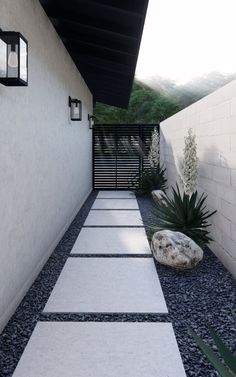 an outdoor walkway leading to a house with white walls and black shinning on the side