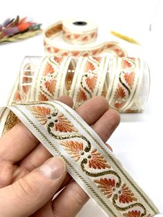 a hand holding a roll of white and orange ribbon with designs on it, along with other items