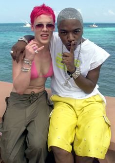 a man and woman sitting on a wall near the ocean with their arms around each other