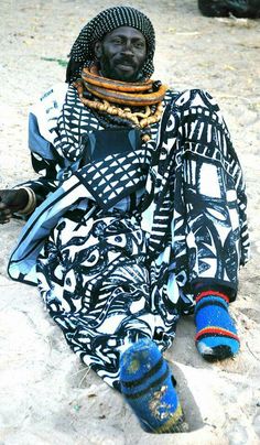 a man sitting on the ground wearing a scarf and hat with his feet in the sand