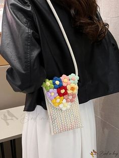 a woman wearing a black jacket and white skirt holding a purse with colorful flowers on it