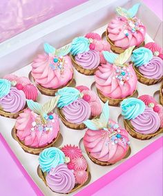 cupcakes with pink, blue and purple frosting in a box on a table