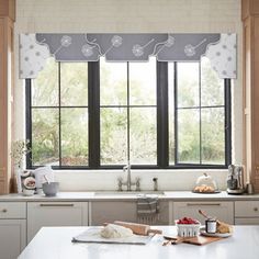 a kitchen with white counter tops and black window curtains over the windows, along with an island in front of it