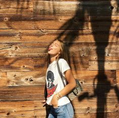 a woman standing in front of a wooden wall with her eyes closed and hands behind her back