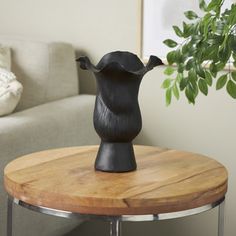 a black vase sitting on top of a wooden table next to a white couch in a living room