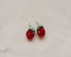 two crocheted strawberries are hanging from silver earwires on a white surface