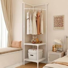 a white shelf with clothes hanging on it next to a window and a bed in a room