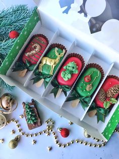 four decorated cupcakes in a box on a table with christmas decorations around them