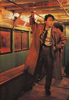 a man standing on a subway train holding onto his coat and looking at the camera