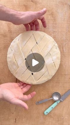 two hands holding a piece of bread on top of a wooden table next to utensils