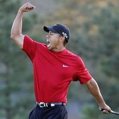 a man in red shirt and black pants holding a golf club with his arm up