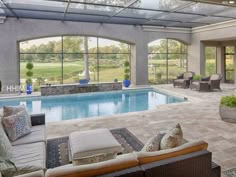 an indoor swimming pool with couches and chairs around it in front of large windows