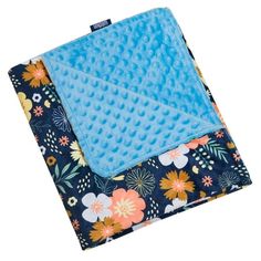 the blue blanket is laying on top of it's flowery print coverlet