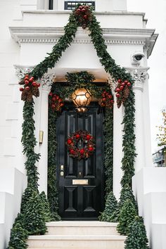 a black front door decorated with christmas wreaths and poinsettia garland on the steps