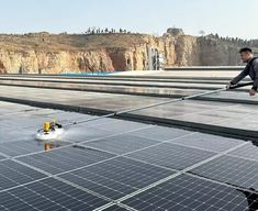 a man is spraying water on the roof of a solar power plant that's surrounded by mountains