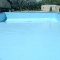 an empty swimming pool with no people around it and trees in the backround