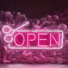 a neon sign that reads open with scissors and feathers in the foreground, against a dark background