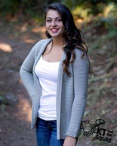 a woman standing in the woods wearing a cardigan sweater and jeans with her hands on her hips