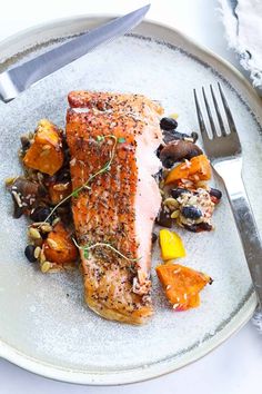 a white plate topped with fish and vegetables next to a fork on top of a table