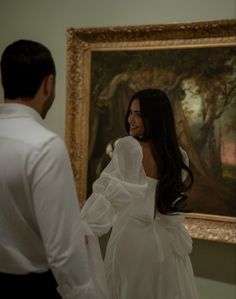 a man and woman standing in front of a painting looking at each other's back