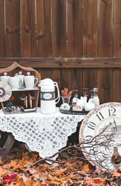 a table topped with plates and cups next to a wooden fence covered in fall leaves