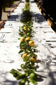 the long table is set with lemons and greenery for an elegant dinner party