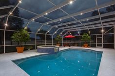 an indoor swimming pool surrounded by glass walls and ceiling lights at night with patio furniture in the foreground