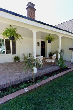 a white house with two chairs and potted plants on the front porch, next to a brick walkway