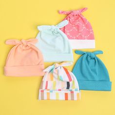 four baby hats with bows on them are lined up against a bright yellow background,